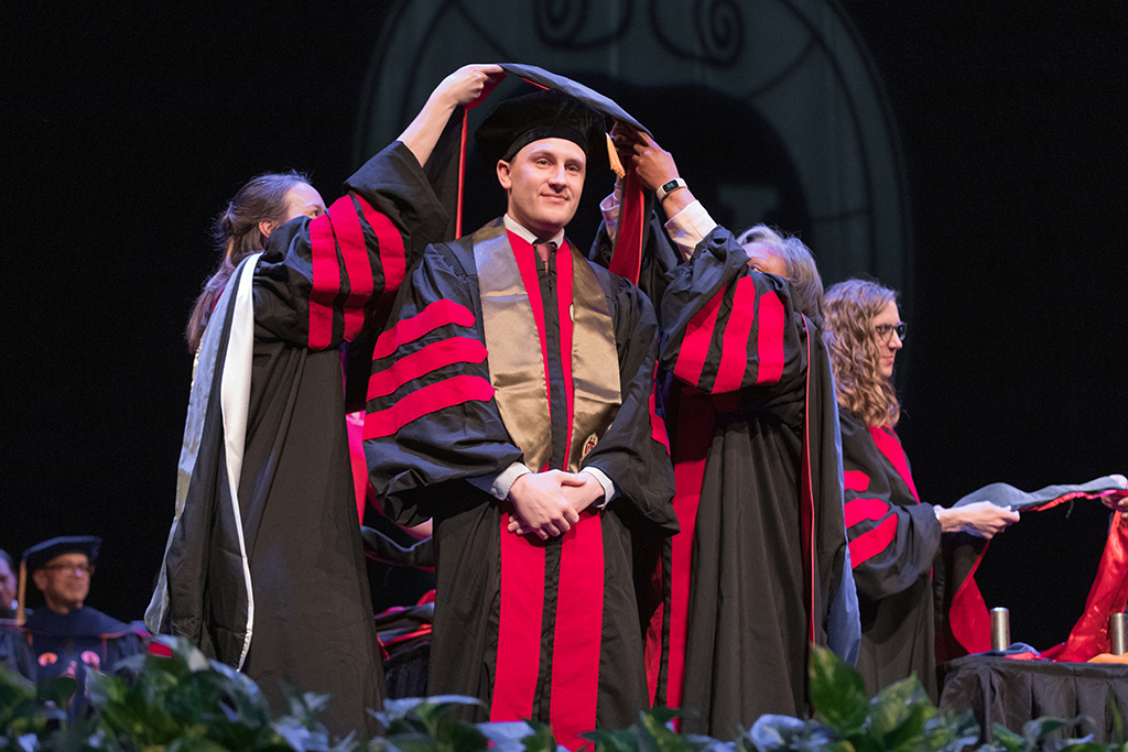 Faculty place a hood over a graduate's head.