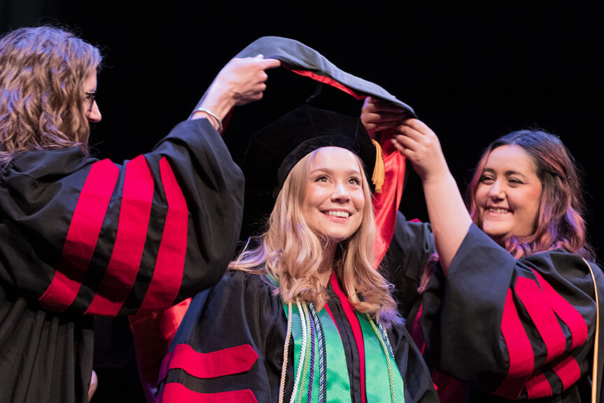 Faculty place a hood over a graduate's head.
