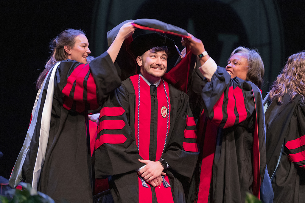Faculty place a hood over a graduate's head.