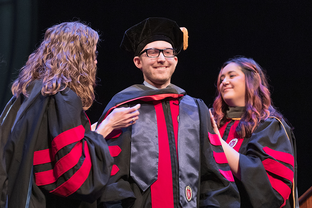 Faculty place a hood over a graduate's head.