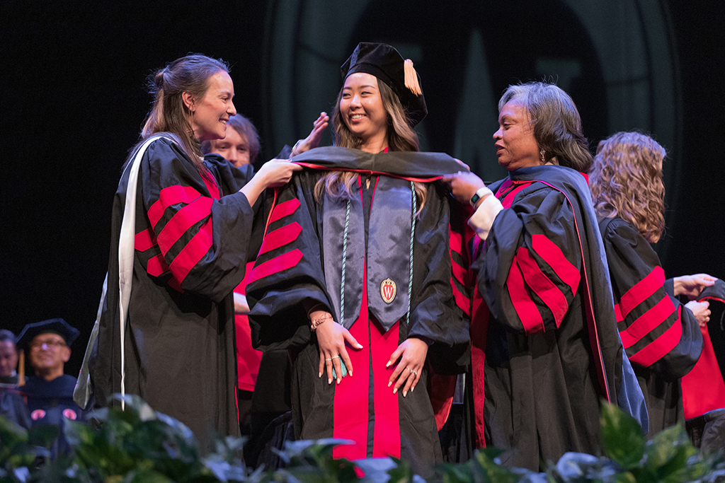 Faculty place a hood over a graduate's head.