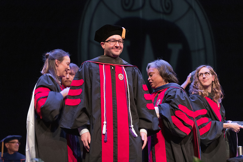 Faculty place a hood over a graduate's head.
