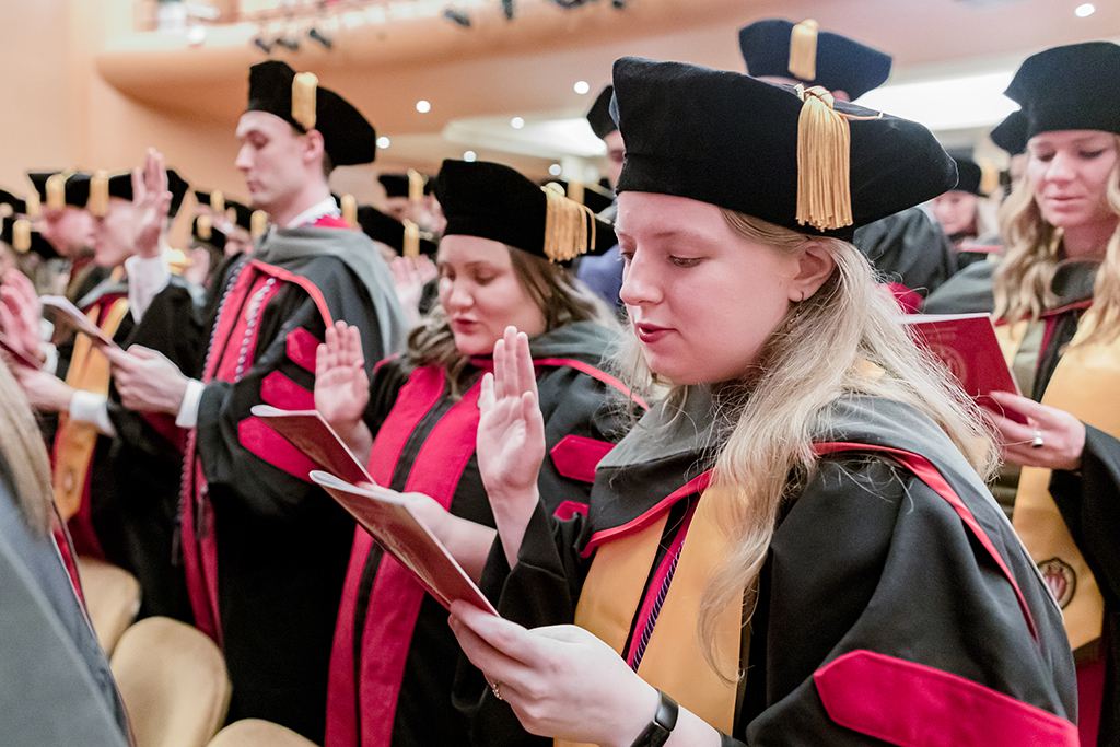 Graduates with one hand raised say the Oath of the Pharmacist.