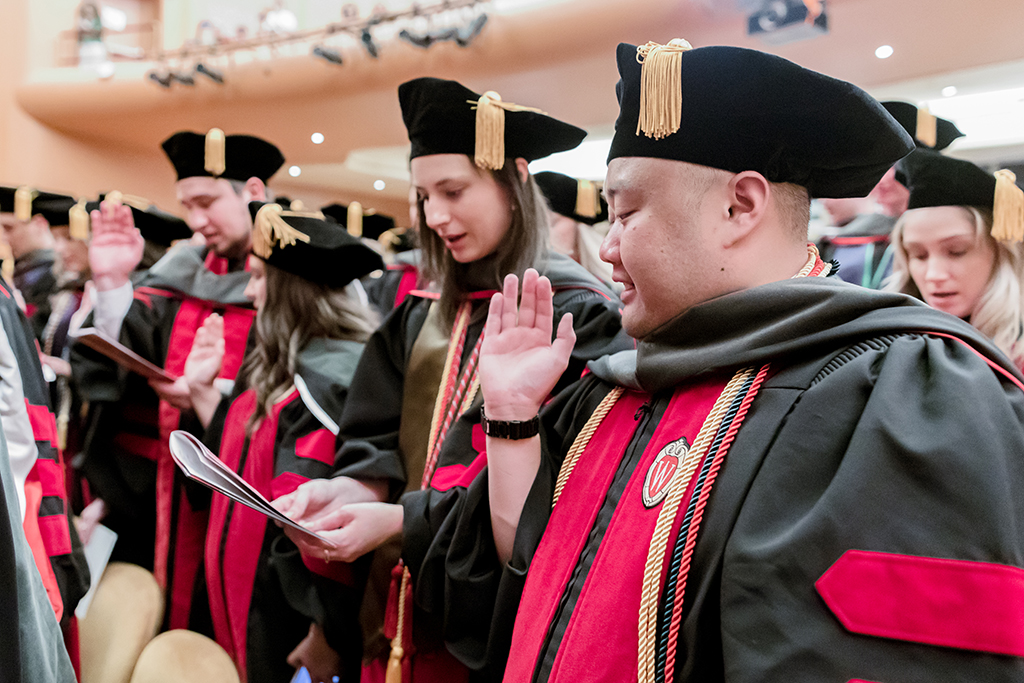 Graduates with one hand raised say the Oath of the Pharmacist.