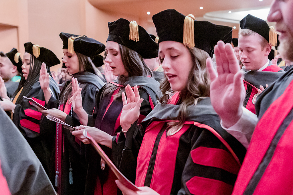 Graduates with one hand raised say the Oath of the Pharmacist.
