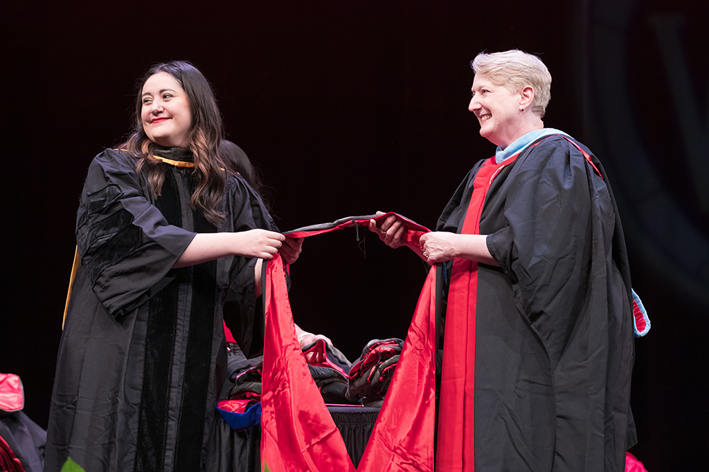 Professors Marina Maes and Karen Kopacek await the next PharmD graduate to hood