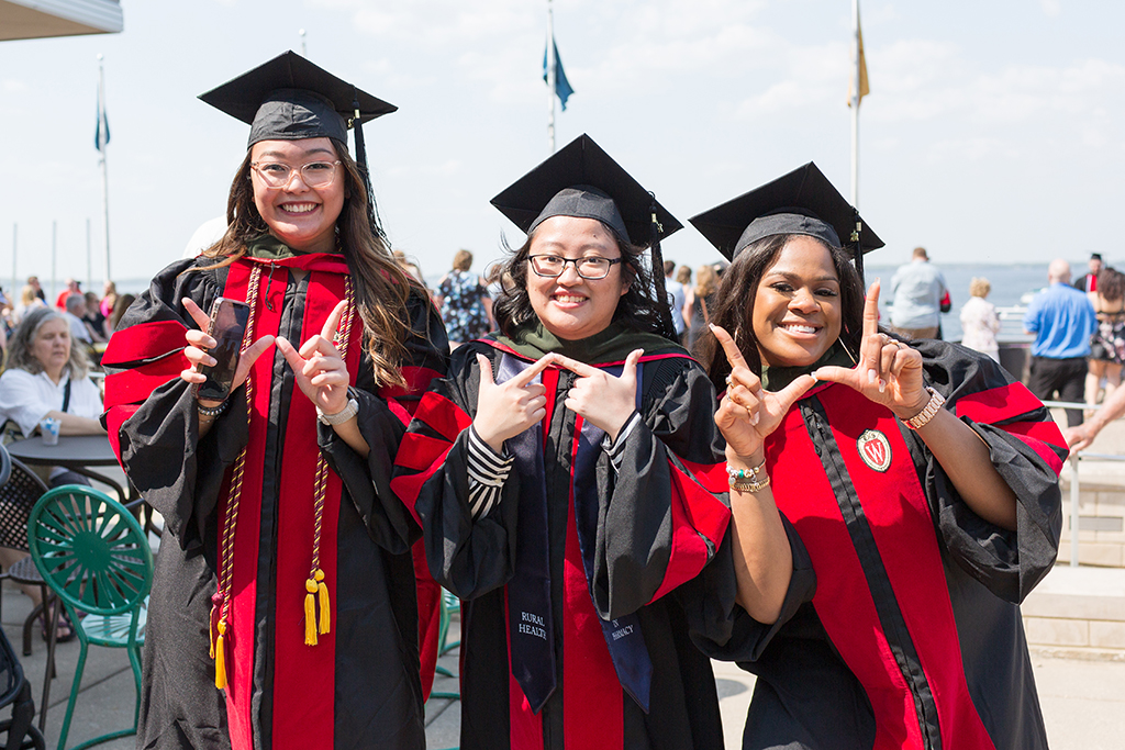 PharmD graduates Lorewell Buaya, Kathy Chao, and Silvya Velez Pache pose together with W hand gestures at Memorial Union Terrace following the 2022 Hooding Ceremony.