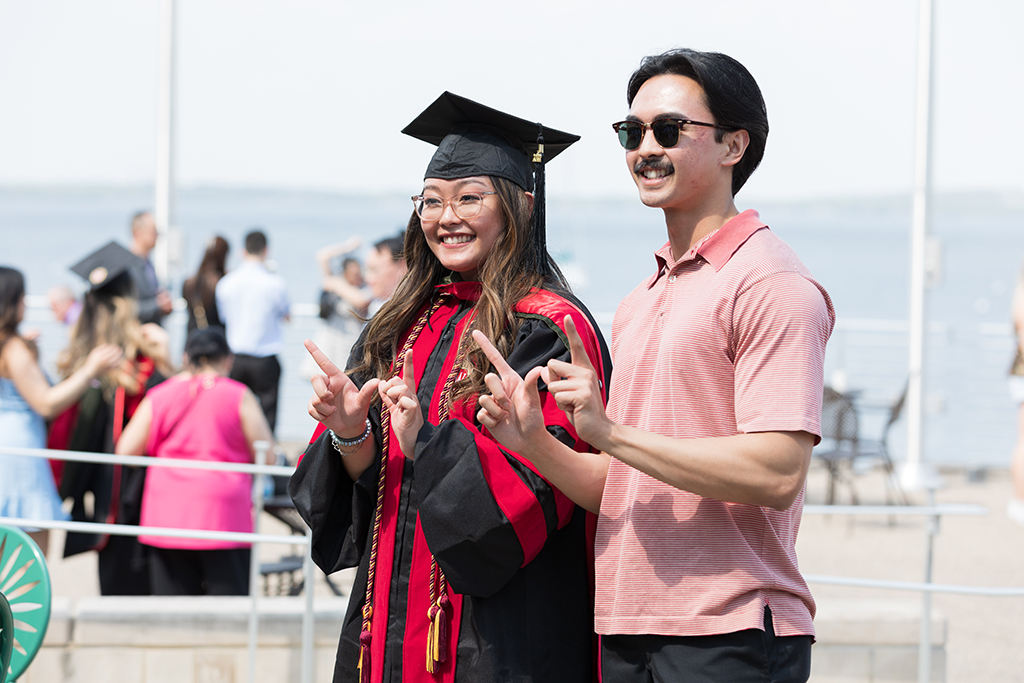 Pharmacy student Lorewell Buaya in cap and gowl poses with a family member by Lake Mendota