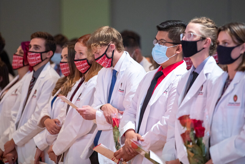 Pharm students holding roses and white coat ceremony pamphlets