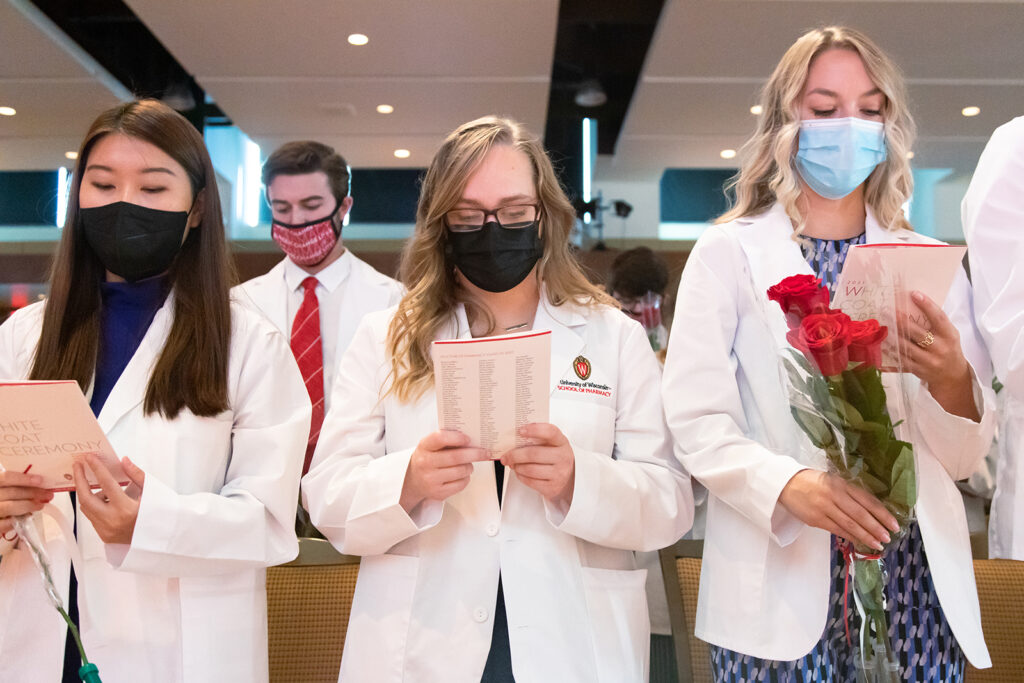 Pharm students holding roses and white coat ceremony pamphlets
