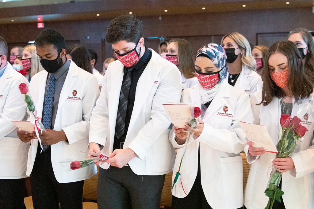 Pharm students holding roses and white coat ceremony pamphlets