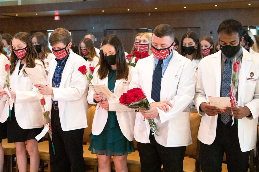 Pharm students holding roses and white coat ceremony pamphlets
