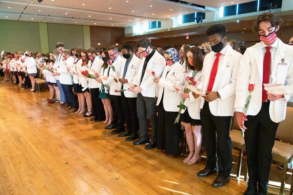 Pharm students holding roses and white coat ceremony pamphlets