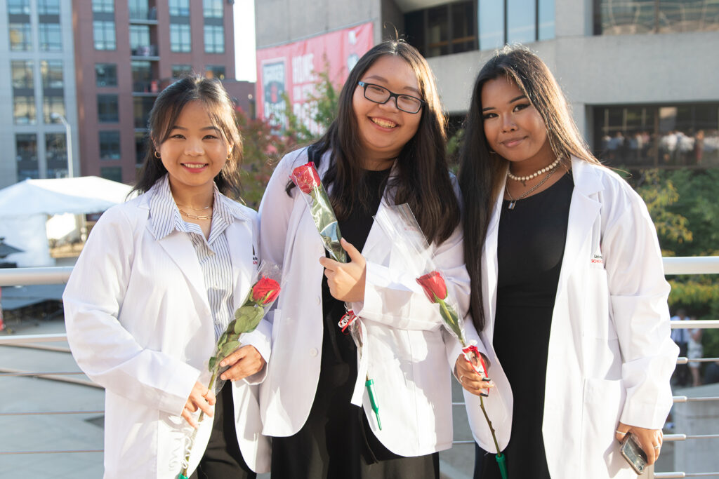 Pharm students together holding roses and wearing their white coats after white coat ceremony