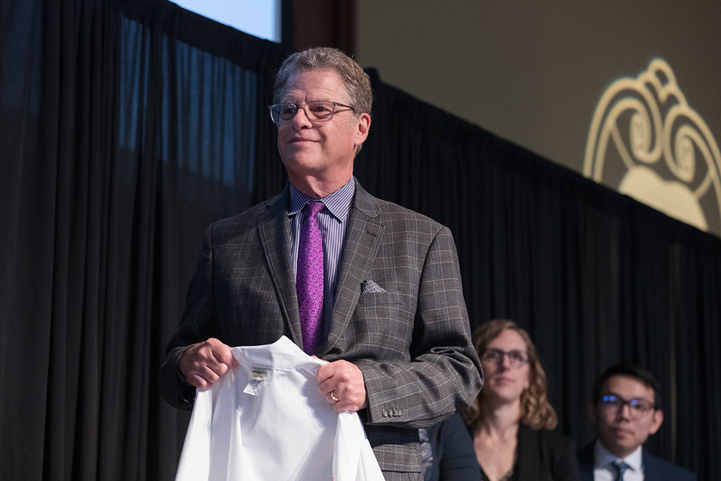 Professor Barry Gidal holds a white coat for a student.