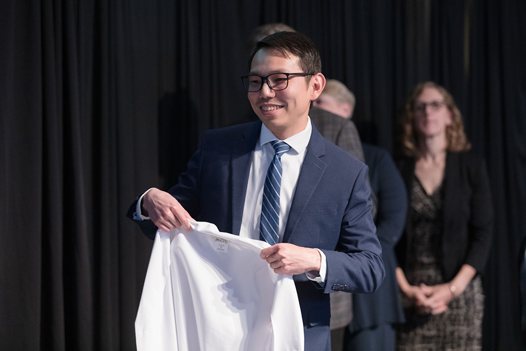 Assistant Professor Sin Yin Lim holds a white coat for a student.