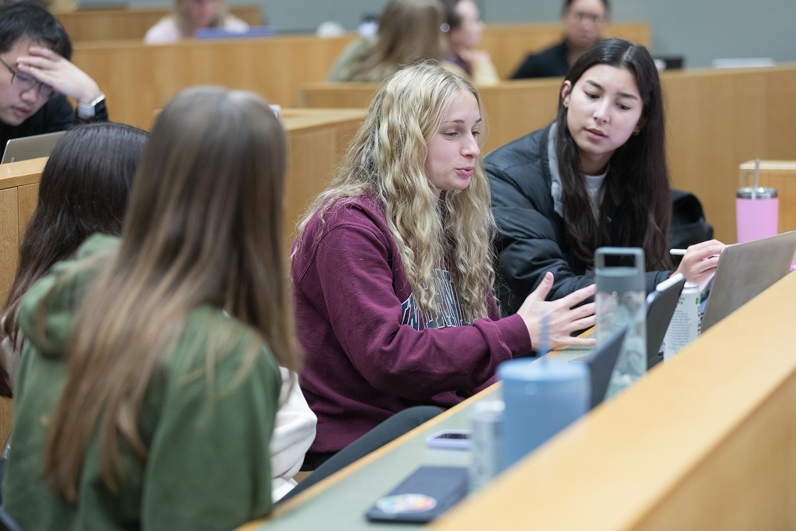 Three students sitting in a lecture hall discuss together