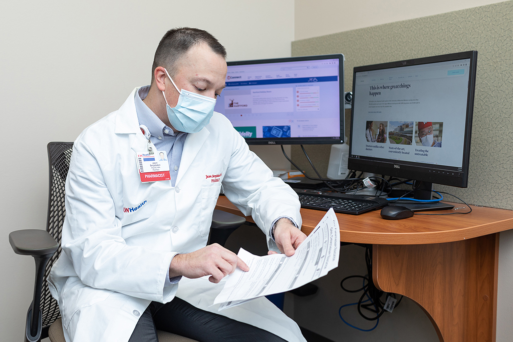 Jason Bergsbaken in a white coat, reviewing papers at a computer