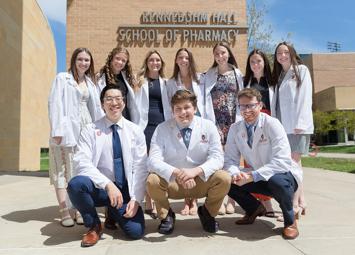 Tenn Class of 2025 PharmD students pose together in their white coats outside Rennebohm Hall following their pinning ceremony.